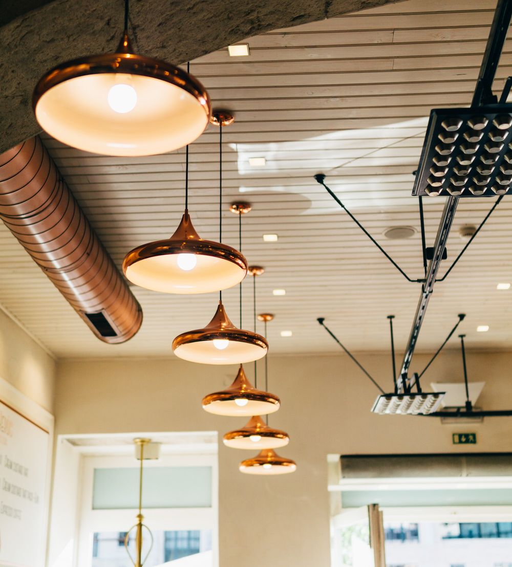 A restaurant with ample lighting provided by a central ceiling light and various hanging lamps throughout the room.